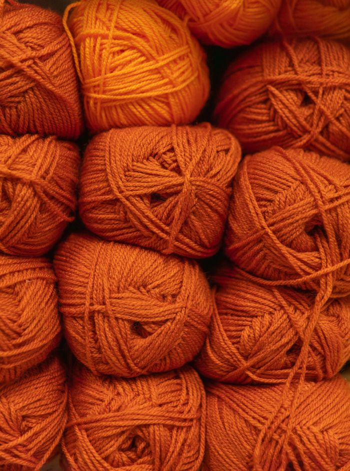 A collection of bright orange wool yarn balls neatly stacked, showcasing texture.