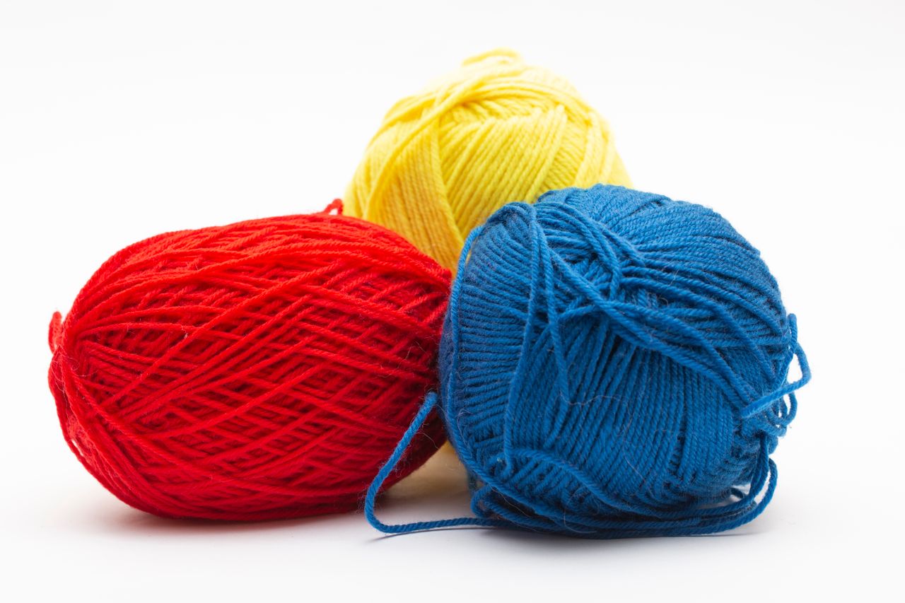 Three vibrant yarn balls in red, yellow, and blue on a white background.